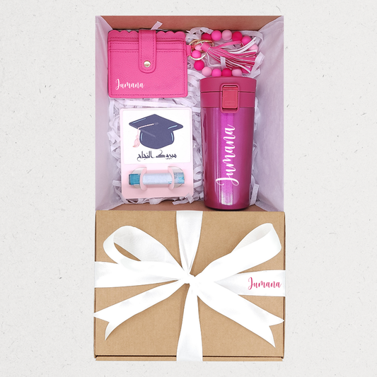 Gift set with pink tumbler, card, and pouch in a box with a white bow.